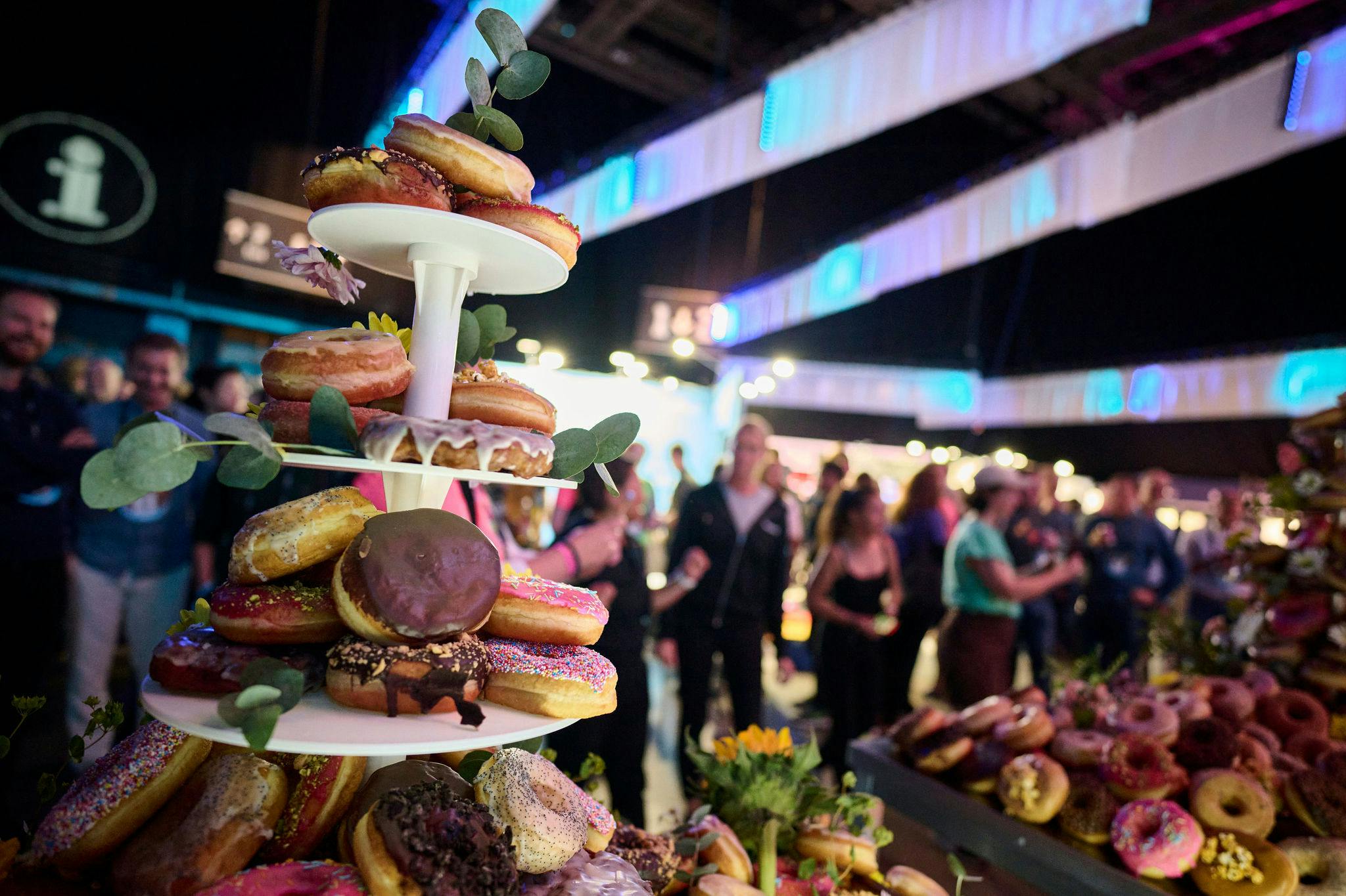 A lot of donuts on tables with people in the background